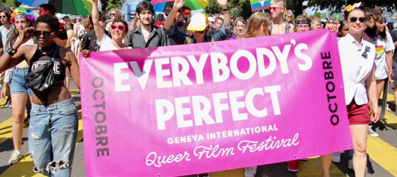 foule en manifestation tenant une banderole rose avec "Everybody's perfect" inscrit dessus