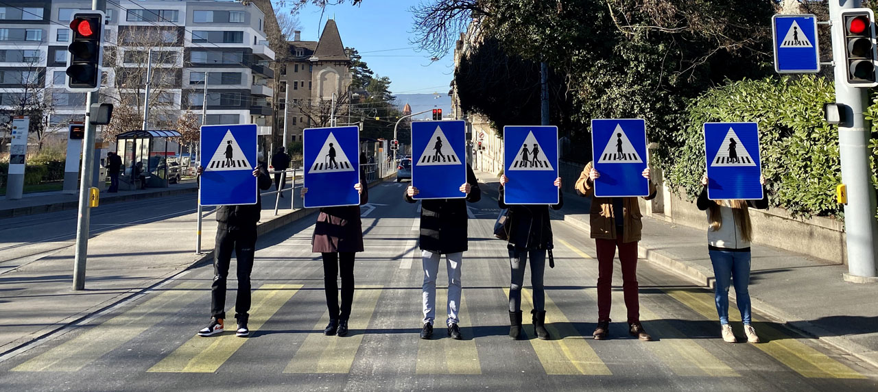 Des gens tiennent les nouveaux panneaux de signalisation routière féminisés sur un passage piétons