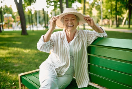Une femme agée assise sur un banc avec un chapeau