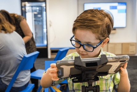 enfant à lunettes qui tient une tablette numérique