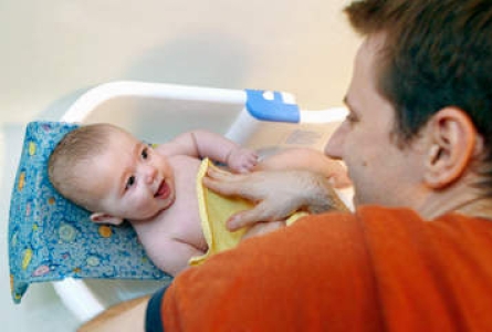 Un homme fait prendre son bain à un bébé souriant.