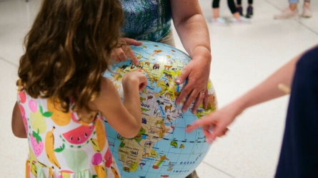 Une petite fille regarde une mappemonde et une adulte lui pointe un pays
