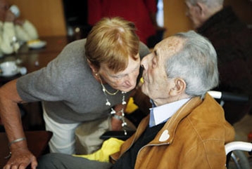 Homme âgé assis qui parle à l'oreille d'une femme qui se penche pour entendre ce qu'il dit