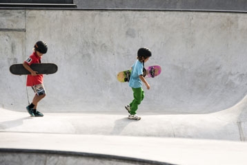 deux enfants casqués dans un bowl, tenant leur skate sous le bras