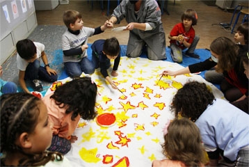 enfants par terre qui peignent sur une grande toile des étoiles