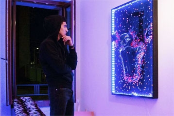 Jeune qui se tient devant une oeuvre lumineuse accrochée au mur