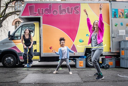 une petite fille et deux femmes posent de façon drôle et enjoué devant un ludobus