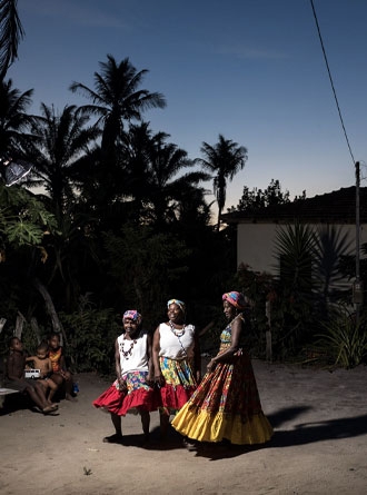 Trois femmes brésiliennes aux jupes colorées dansent dans la nuit qui tombe.