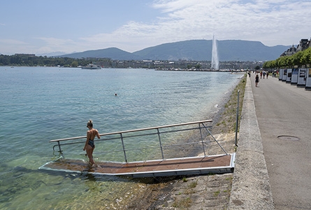 femme en maillot qui descend une rampe donnant sur l'eau. Au loin, le jet d'eau de Genève