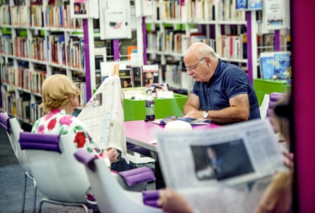 Seniors dans une bibliothèque, attablés et lisant le journal