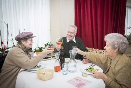 3 personnes âgées autour d'une table, trinquant avec leur verre