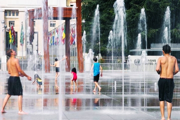 jets d'eau allumés sur la place des Nations, sur laquelle jouent enfants et adultes en maillot de bain