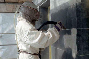 Un peintre en bâtiment vaporise un mur avec un masque de protection.