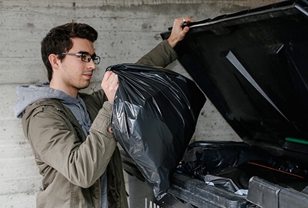 Un jeune homme jette un sac poubelle dans un container