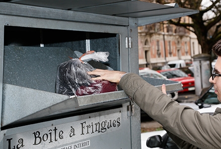 Un jeune homme jette un sac d'habits dans un container spécialisé