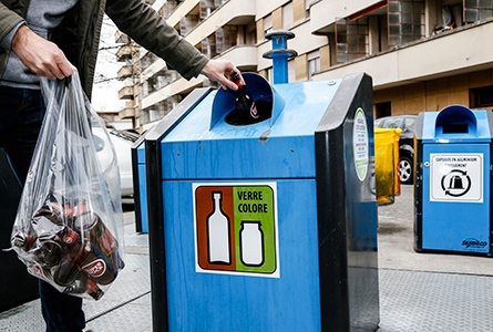 Une personne jette des bouteilles en verre dans un container spécialisé