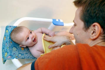 Un homme fait prendre son bain à un bébé souriant.