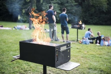 barbecue avec  des flammes, dans un parc. Au loin, des personnes sont dans l'herbe