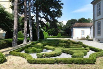 jardin à la française bordé d'un côté d'arbres dont on ne voit presque que les troncs, et d'une maison de maître de l'autre côté