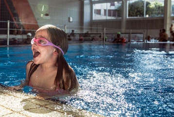 jeune fille avec lunettes de natation qui sort son buste de l'eau