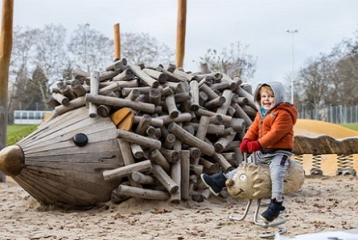 jeune garçon habiellé en habits d'hiver, dehors, devant un jeu en bois en forme de hérisson