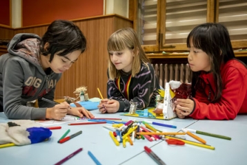 enfants appuyés sur une table jonchée de crayons de couleurs