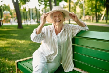 Une femme agée assise sur un banc avec un chapeau