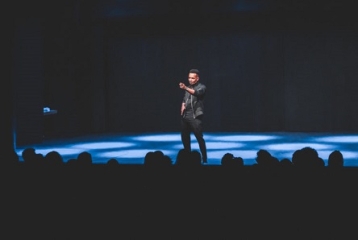 homme en blouson noir seul sur une scène avec fond noir